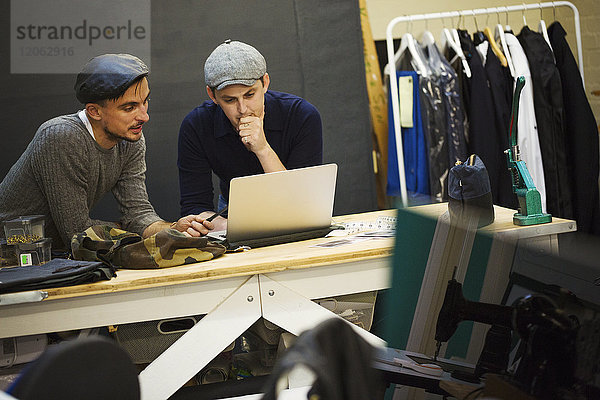 Zwei Männer arbeiten an einem Laptop und teilen sich den Bildschirm. Eine Schneiderei-Werkstatt