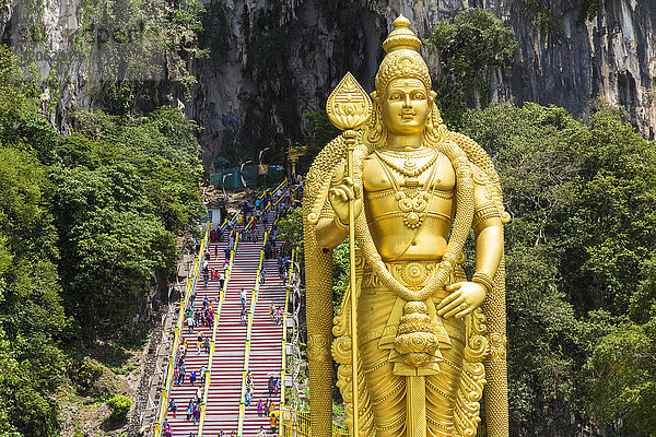 Kolossale goldene Statue einer hinduistischen Gottheit  mit einer Treppe in eine Höhle im Hintergrund.