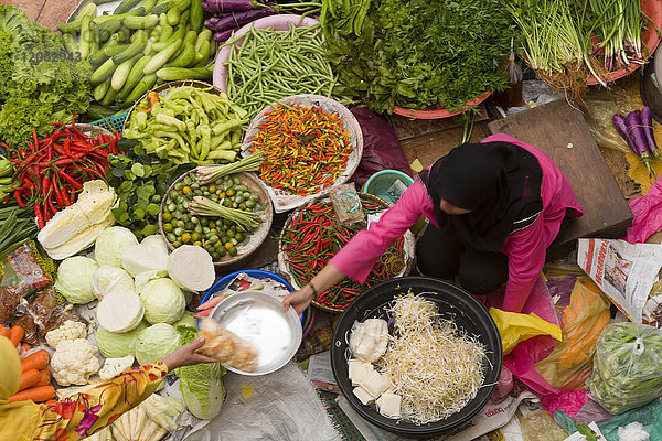 Schrägaufnahme eines Verkäufers  der eine Auswahl an frischem Gemüse auf einem Straßenmarkt verkauft.