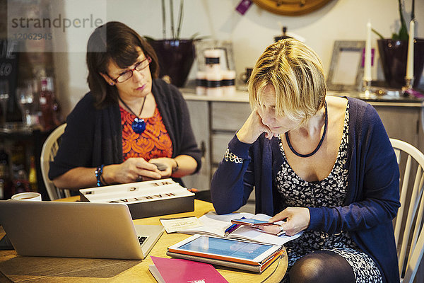 Zwei Frauen saßen an einem Tisch  eine benutzte ein Smartphone und schaute auf einen Laptop-Bildschirm.