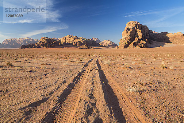 Wüstenlandschaft mit Reifenspuren  die zu einem entfernten Berg führen.