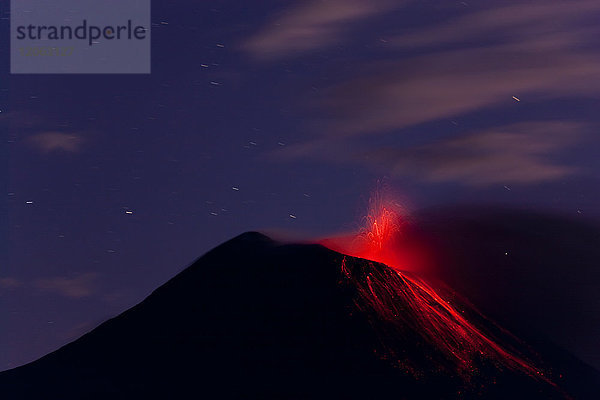 Abends Blick auf den feurigen Ausbruch des Vulkans  bei dem Lava die Berghänge hinunterfließt.