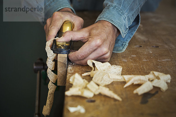 Ein Handwerker hält einen Speichenrasierer und formt damit ein Stück Holz in einer Klemme.