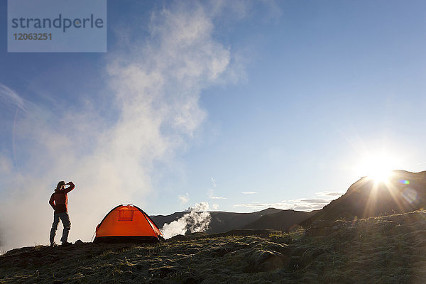 Frau steht in den Bergen  neben einem Zelt  Sonnenaufgang.