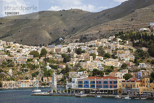 Kleinstadt mit Häusern und Hafenpromenade an einem Berghang im Mittelmeer.
