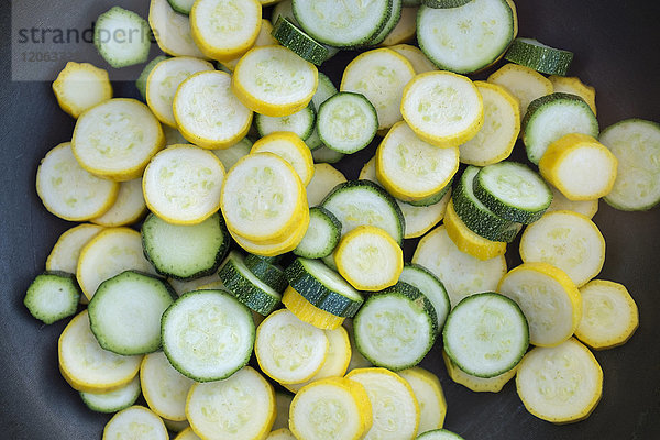 In Scheiben geschnittenes frisches Zucchini-Zucchinigemüse mit grüner und gelber Schale in einer Pfanne.