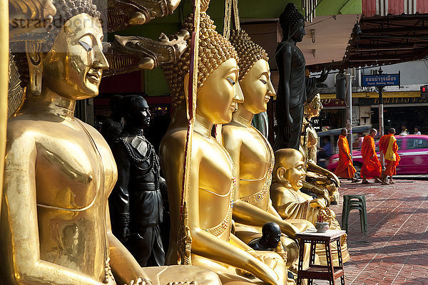 Hohe goldene Buddha-Statuen  die auf einem Bürgersteig aufgereiht sind.