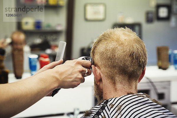 Ein Kunde sitzt auf dem Stuhl des Barbiers  und ein Barbier rasiert sich den Kopf mit einem Elektrorasierer.