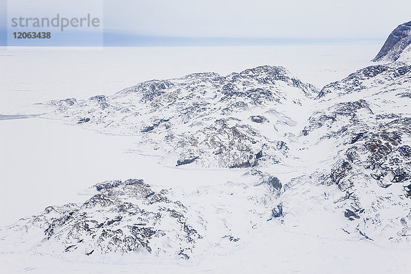 Hochwinkelaufnahme einer felsigen  mit Schnee und Eis bedeckten Winterlandschaft mit dem Meer in der Ferne.