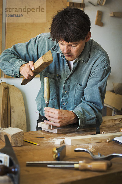 Ein Handwerker  der ein Stück Holz am Ende eines Stemmeisens benutzt  um ein Stück Holz zu markieren.