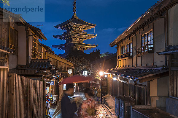 Japanisches Paar in traditioneller Kleidung  das nachts auf einer Straße steht  im Hintergrund eine Pagode.