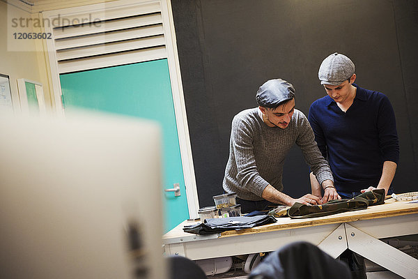 Zwei Männer  Schneider  die sich über eine Werkbank lehnen  um ein Projekt zu besprechen und ihre Arbeit zu planen.