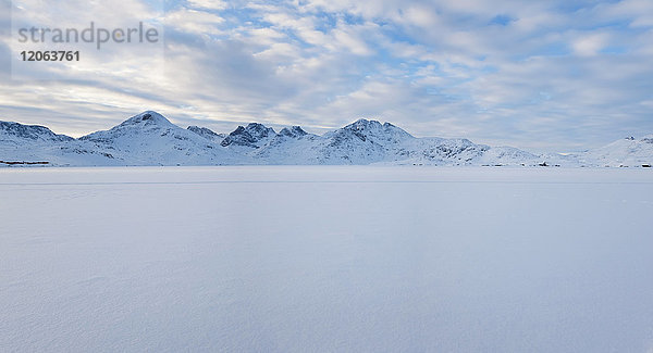 Winterlandschaft unter bewölktem Himmel  mit Bergen in der Ferne.