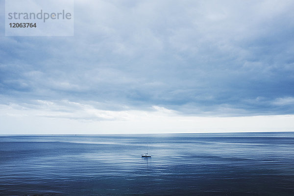 Blick über ein ruhiges Meer bis zum Horizont und einen bewölkten Himmel. Eine kleine Yacht  Tagesboot mit Motorantrieb.