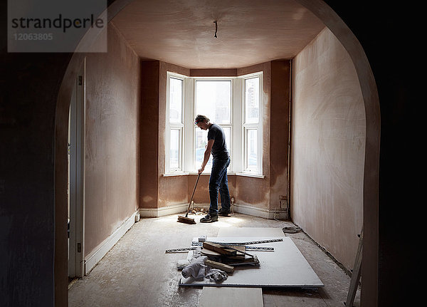 Ein Bauarbeiter beim Fegen und Aufräumen in einem renovierten  neu verputzten Haus mit Bogengang.