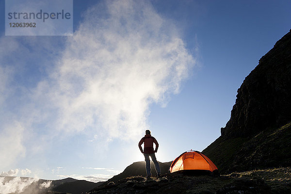 Rückansicht einer Frau  die in den Bergen steht  neben einem Zelt  Sonnenaufgang.