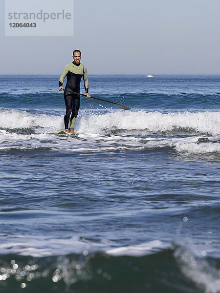 Mann Surfer sehnt sich nach der Spitze der Welle am Strand von Sopelana