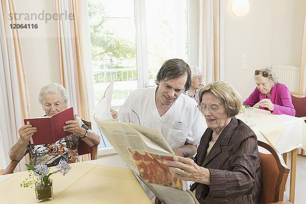 Pflegerin liest Zeitung mit älterer Frau im Altersheim