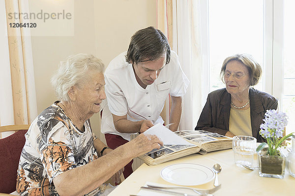 Betreuerin betrachtet Fotoalbum mit älteren Frauen im Altersheim