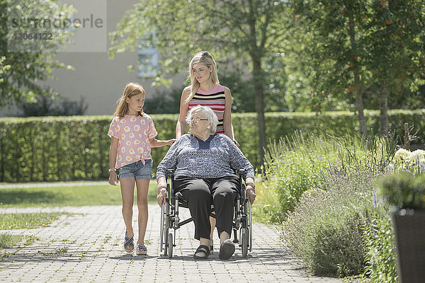 Ältere Frau im Rollstuhl mit Tochter und Enkelin im Altenheimpark