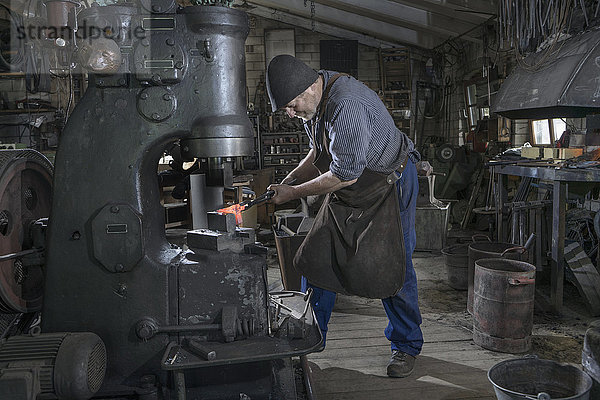 Schmied hämmert rotglühende Eisenstange in Hammermaschine in Werkstatt