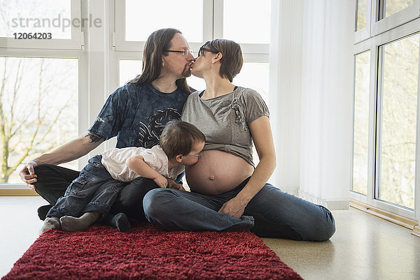 Eltern küssen sich  während der Sohn den Bauch der schwangeren Mutter küsst