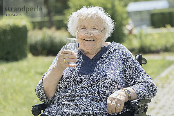 Ältere Frau im Rollstuhl trinkt ein Glas Wasser