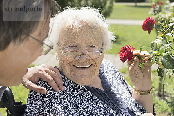 Sohn mit Mutter riecht an Rosenblüten im Park