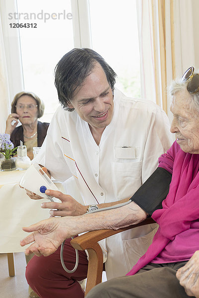 Pfleger kontrolliert Blutdruck einer älteren Frau im Altersheim