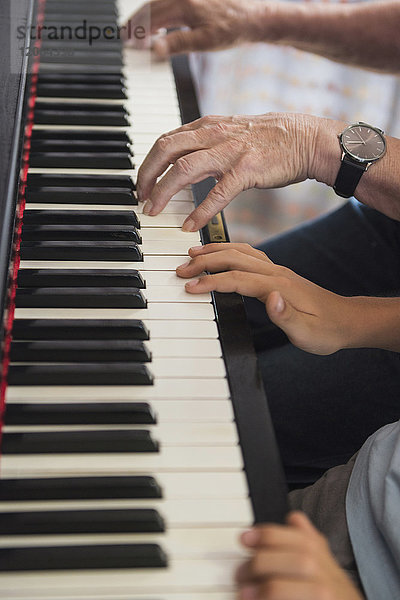 Hände des Großvaters und des Enkels beim Klavierspielen