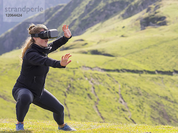 Frau übt Tai-Chi-Bewegungen mit Virtual-Reality-Brille auf einem Berg