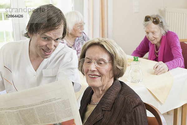 Hausmeisterin liest mit älterer Frau im Altersheim Zeitung