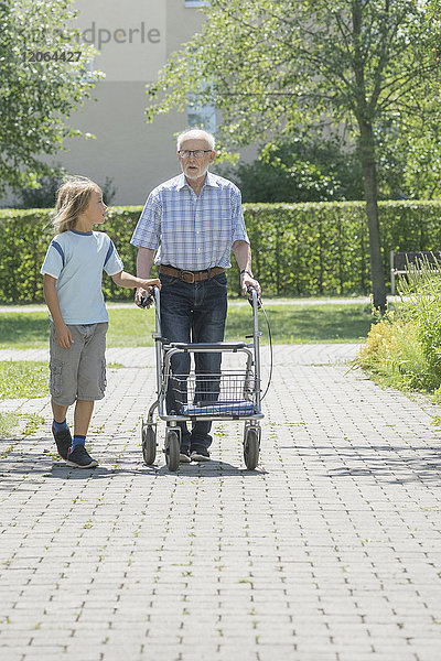 Junge hilft Großvater mit Gehhilfe im Altenheimpark