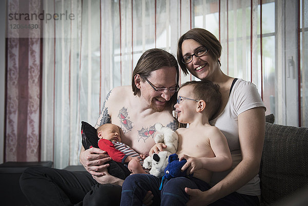Porträt der Eltern mit neugeborenem Baby und kleinem Sohn auf dem Sofa sitzend