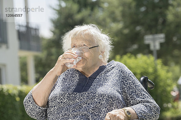 Ältere Frau im Rollstuhl trinkt ein Glas Wasser