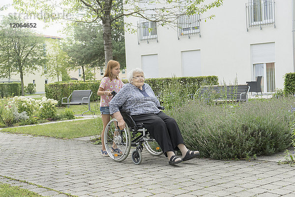 Ältere Frau im Rollstuhl mit Enkelin im Altenheimpark