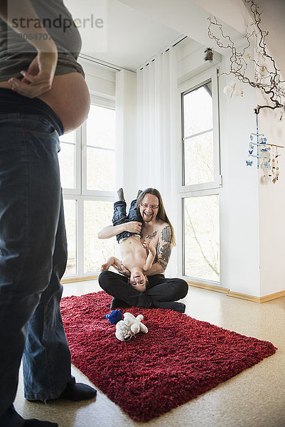 Schwangere Mutter schaut auf Vater und Sohn  die auf dem Teppich spielen
