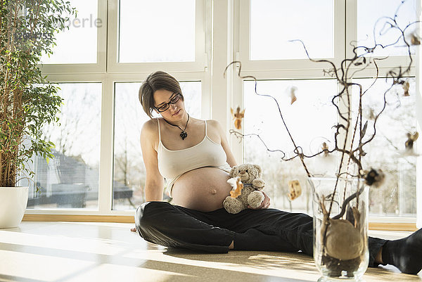 Schwangere Frau mit Teddybär auf dem Boden sitzend