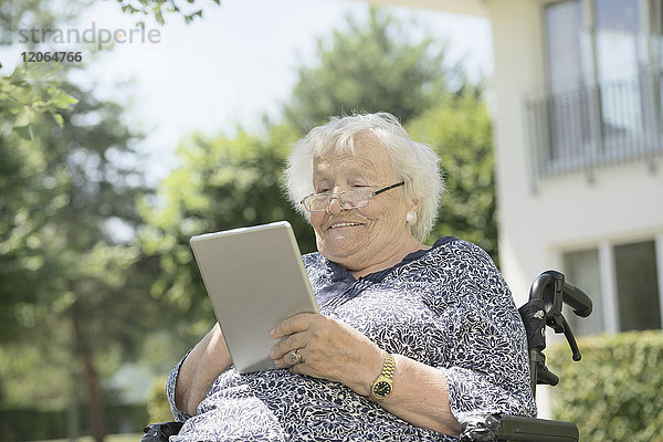 Ältere Frau benutzt digitales Tablet im Rollstuhl