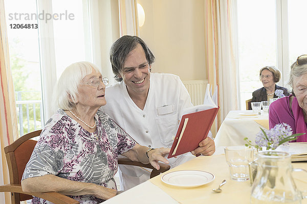 Hausmeisterin liest mit einer älteren Frau im Altersheim ein Buch