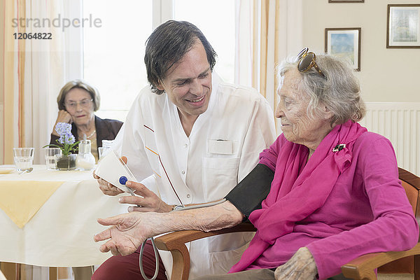 Pflegerin prüft Blutdruck einer älteren Frau im Altersheim