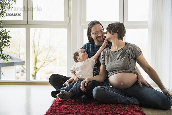 Schwangere Mutter mit Vater und Sohn auf dem Teppich sitzend