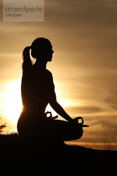 Silhouette einer Frau  die im Licht der Abendsonne Yoga übt. Lotus-Stellung. Französische Alpen. Frankreich.