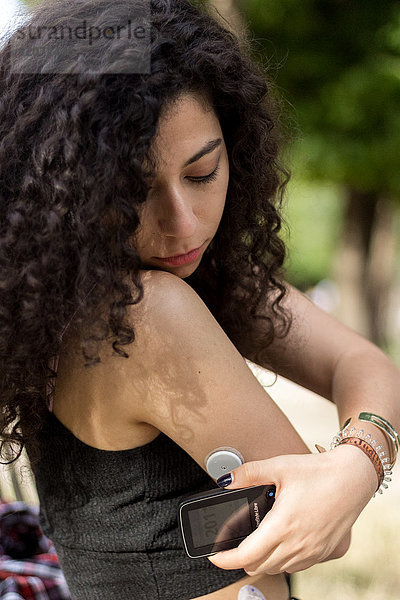 Eine junge Diabetikerin  ausgestattet mit einem Glukosesensor und einem Freestyle Libre Scanner. Der Scanner kann einfach an den Sensor auf der Rückseite des Arms gehalten werden  um den Blutzuckerspiegel sofort zu messen.