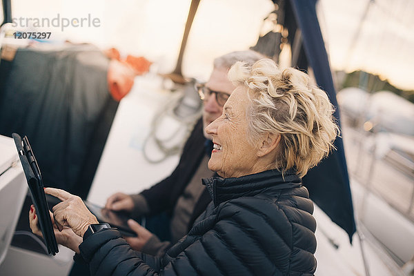 Seitenansicht der lächelnden Seniorin mit digitalem Tablett von Mann in der Yacht