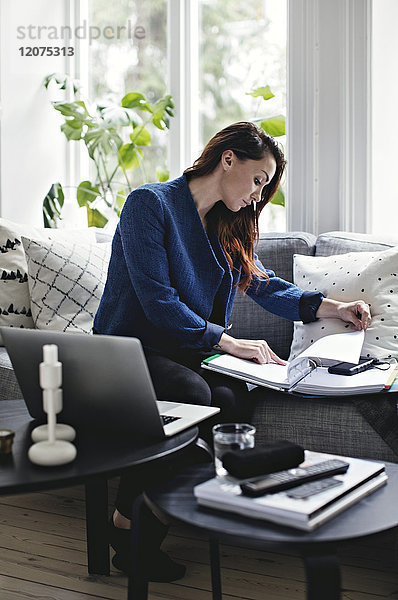 Geschäftsfrau beim Lesen von Dokumenten auf dem Sofa im Home-Office