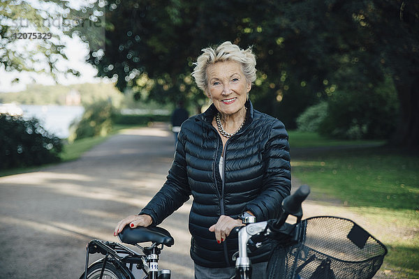 Portrait of smiling senior woman with bicycle in park