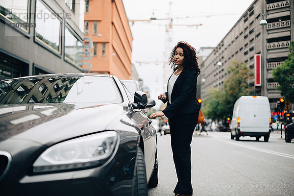 Full length of mid adult businesswoman standing by car on street in city