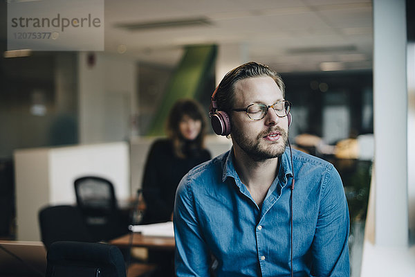 Mid adult businessman listening to headphones with eyes closed at office