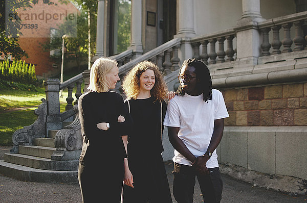 Multi-ethnic male and female students talking while walking by university